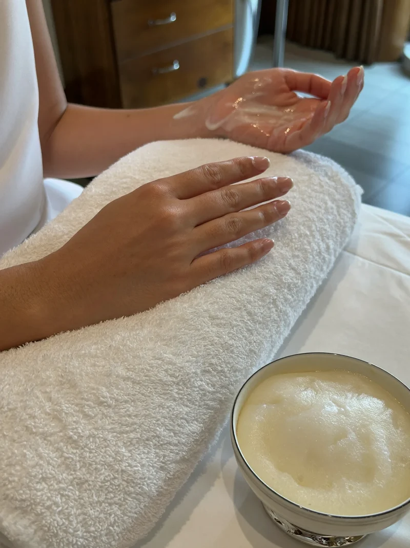 Illustration: Handmassage mit Creme und warmem Tuch neben einer kleinen Paraffinschale